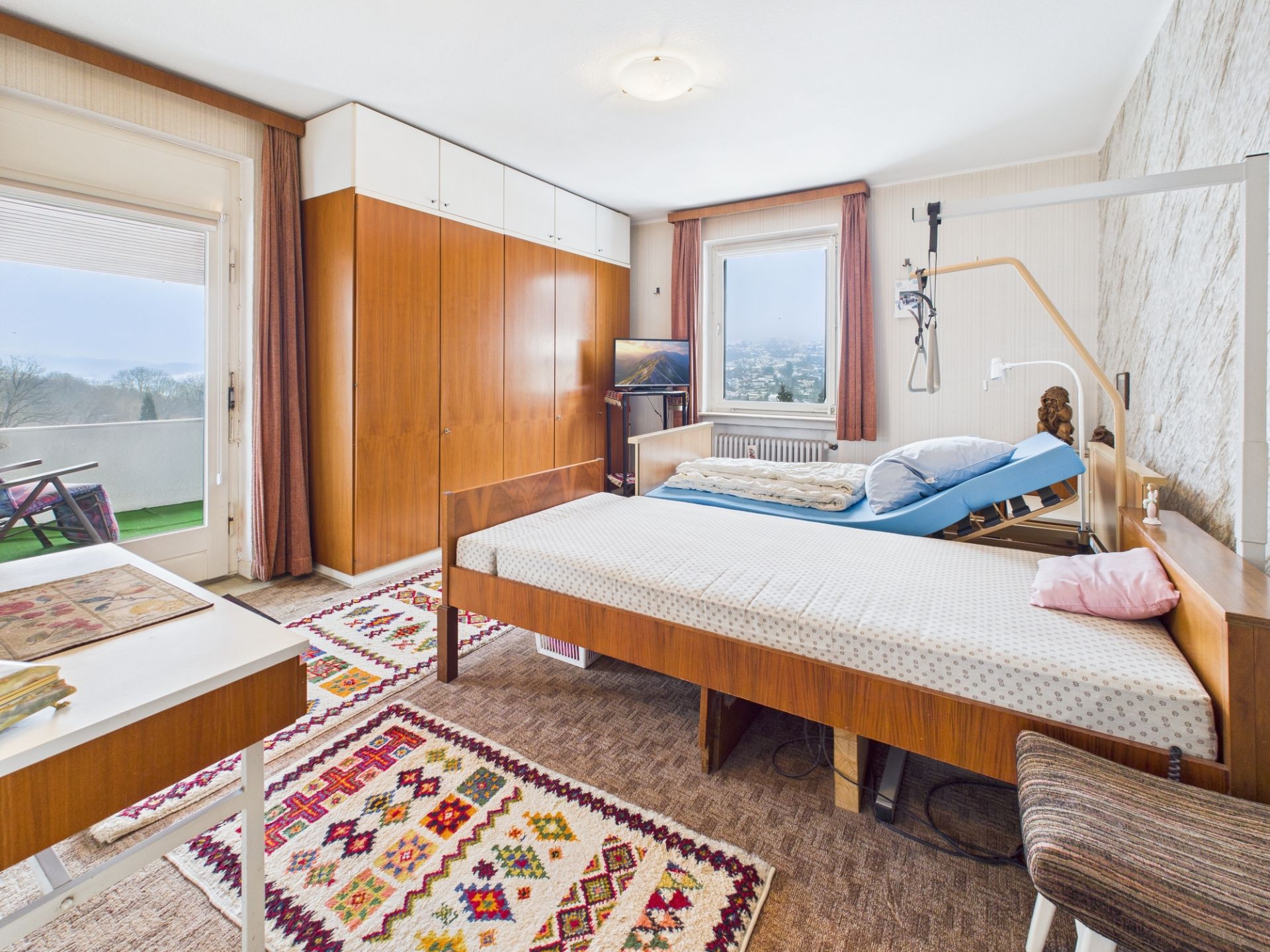 Schlafzimmer mit zwei Betten, großem Schrank, Teppichen und Zugang zu einem Balkon.