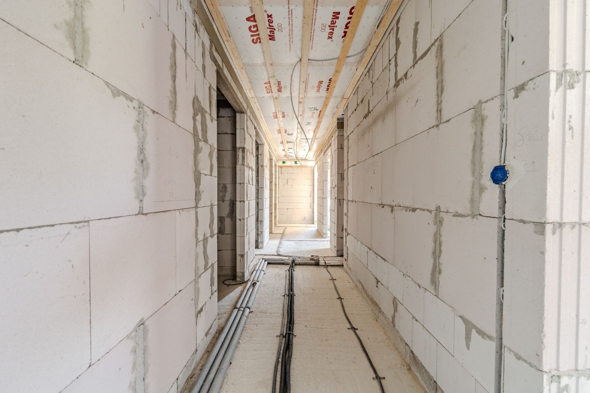 Flur in einem Wohnhaus im Rohbau mit sichtbaren Leitungen und unverputzten Wänden.