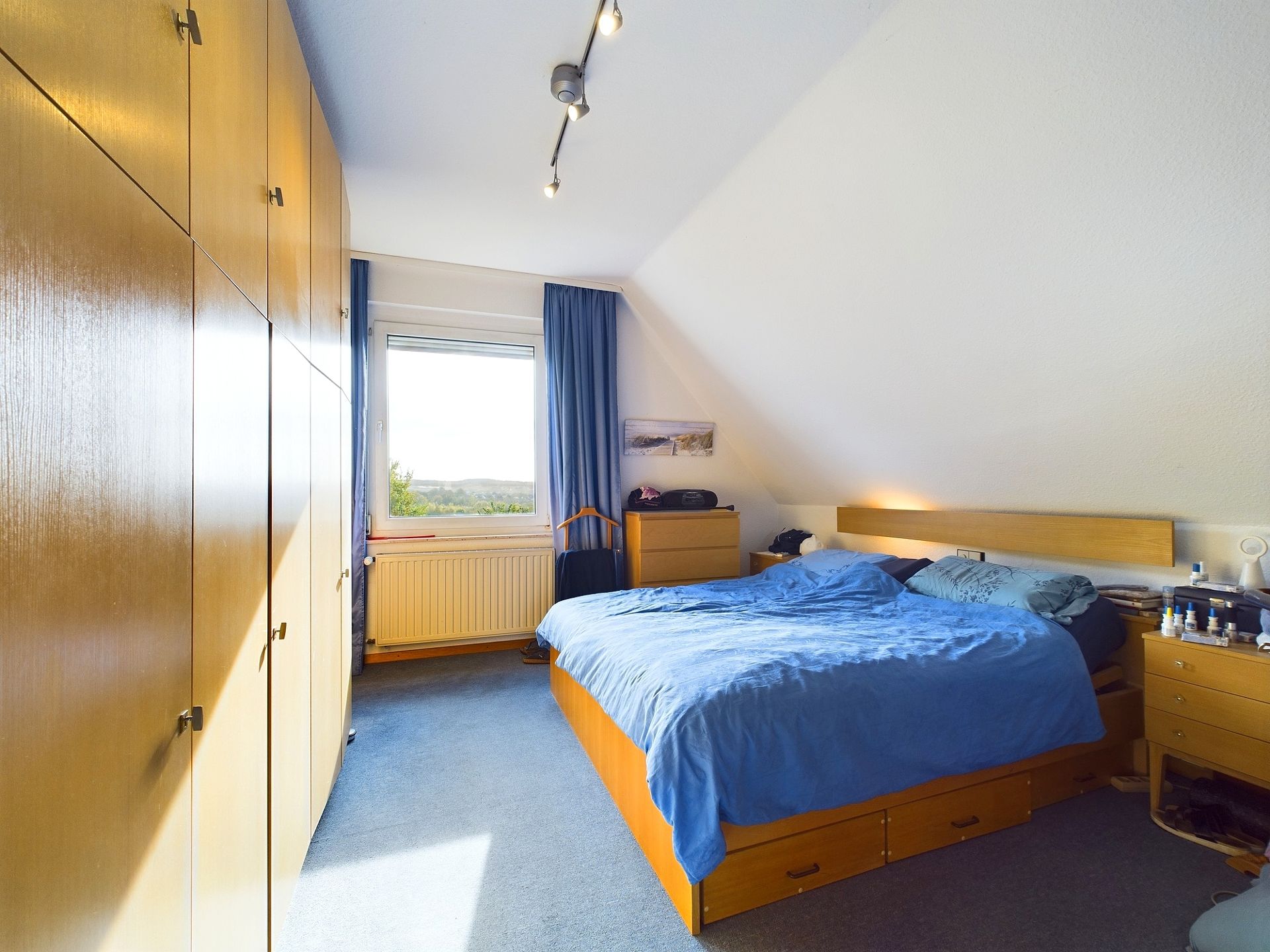 Schlafzimmer mit großem Bett, Holzschränken, Nachttischen und Fenster mit Blick ins Grüne.