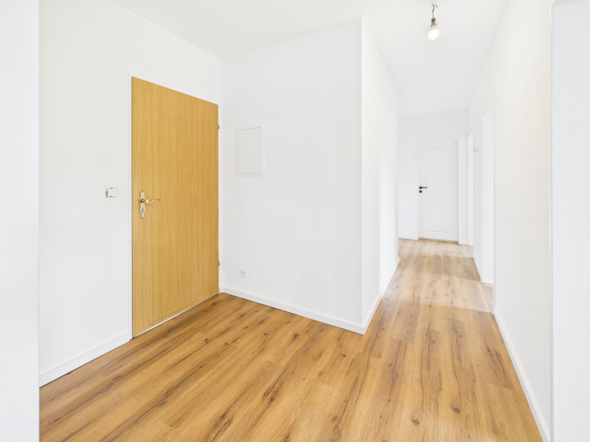 Heller Flur mit Holzboden, weißen Wänden und Holztür in einer Wohnung.