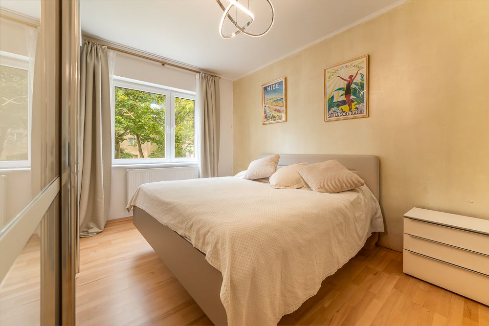Helles Schlafzimmer mit Doppelbett, großem Fenster, Nachttisch und zwei Bildern an der Wand.