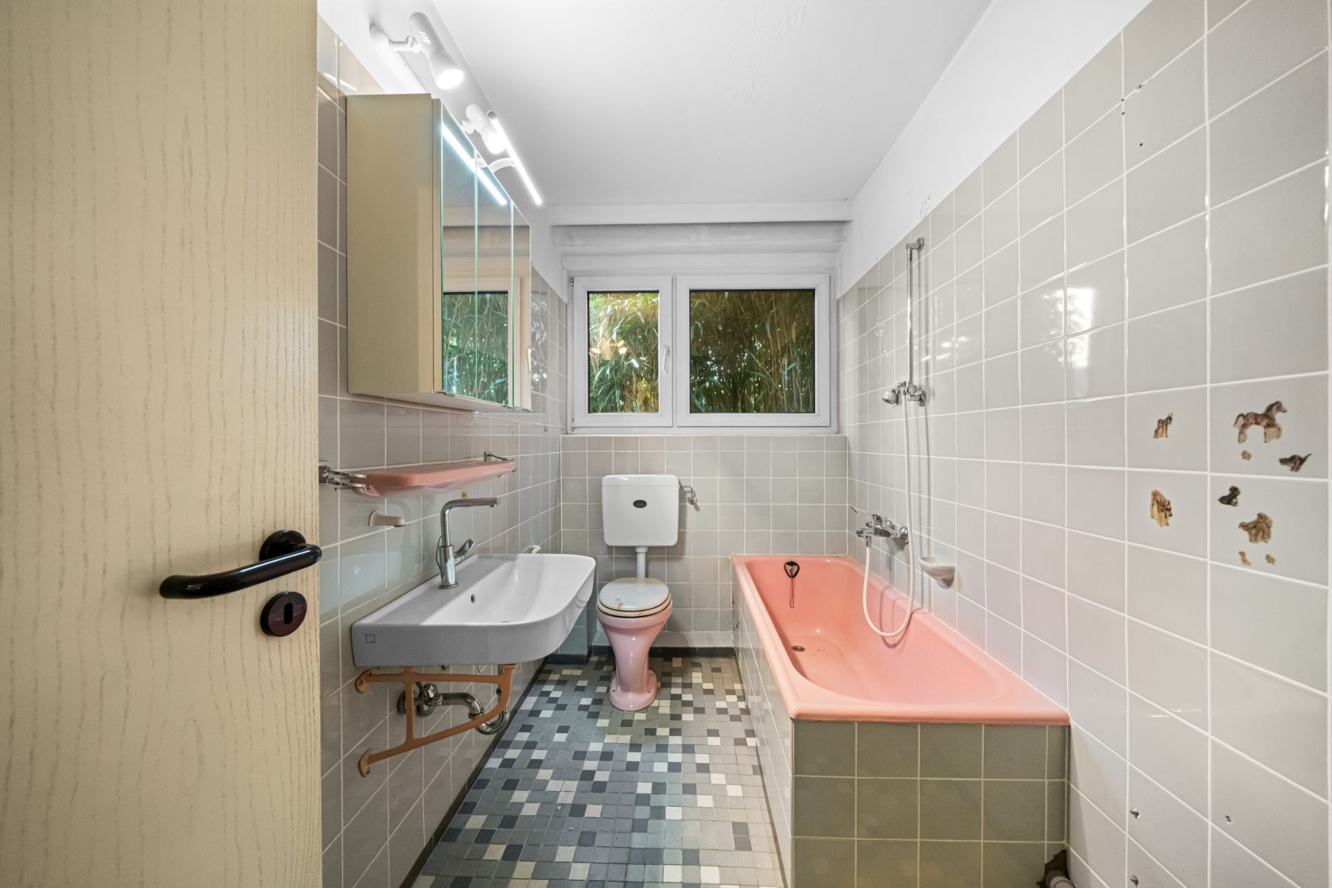 Badezimmer mit rosa Badewanne, Waschbecken, Toilette und zwei Fenstern.