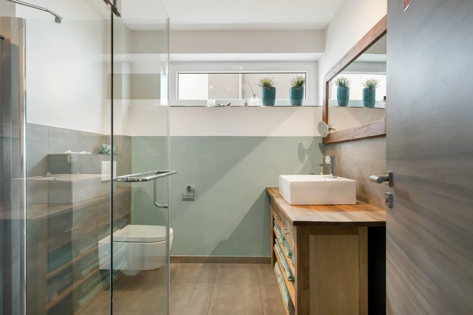 Modernes Badezimmer mit Glasdusche, großem Spiegel, Waschbecken und Pflanzen auf dem Fensterbrett.