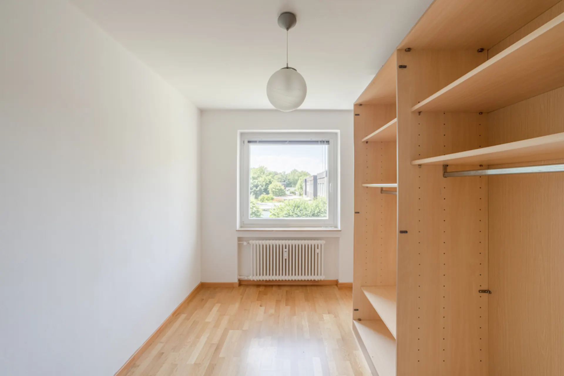 Helles, schmales Zimmer mit Holzregalen, Fenster und Hängelampe.