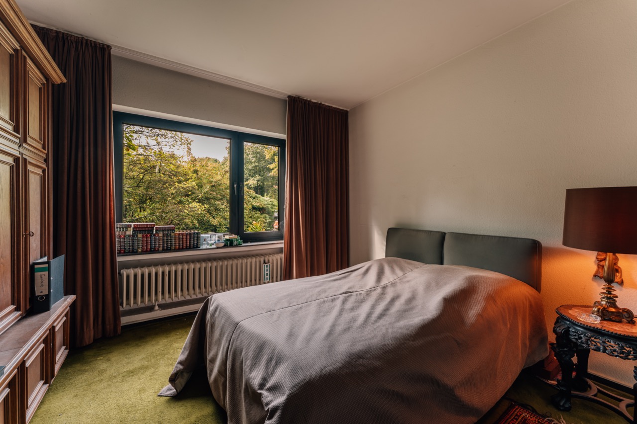 Schlafzimmer mit Doppelbett, großem Fenster, braunen Vorhängen und Nachttisch mit Lampe.