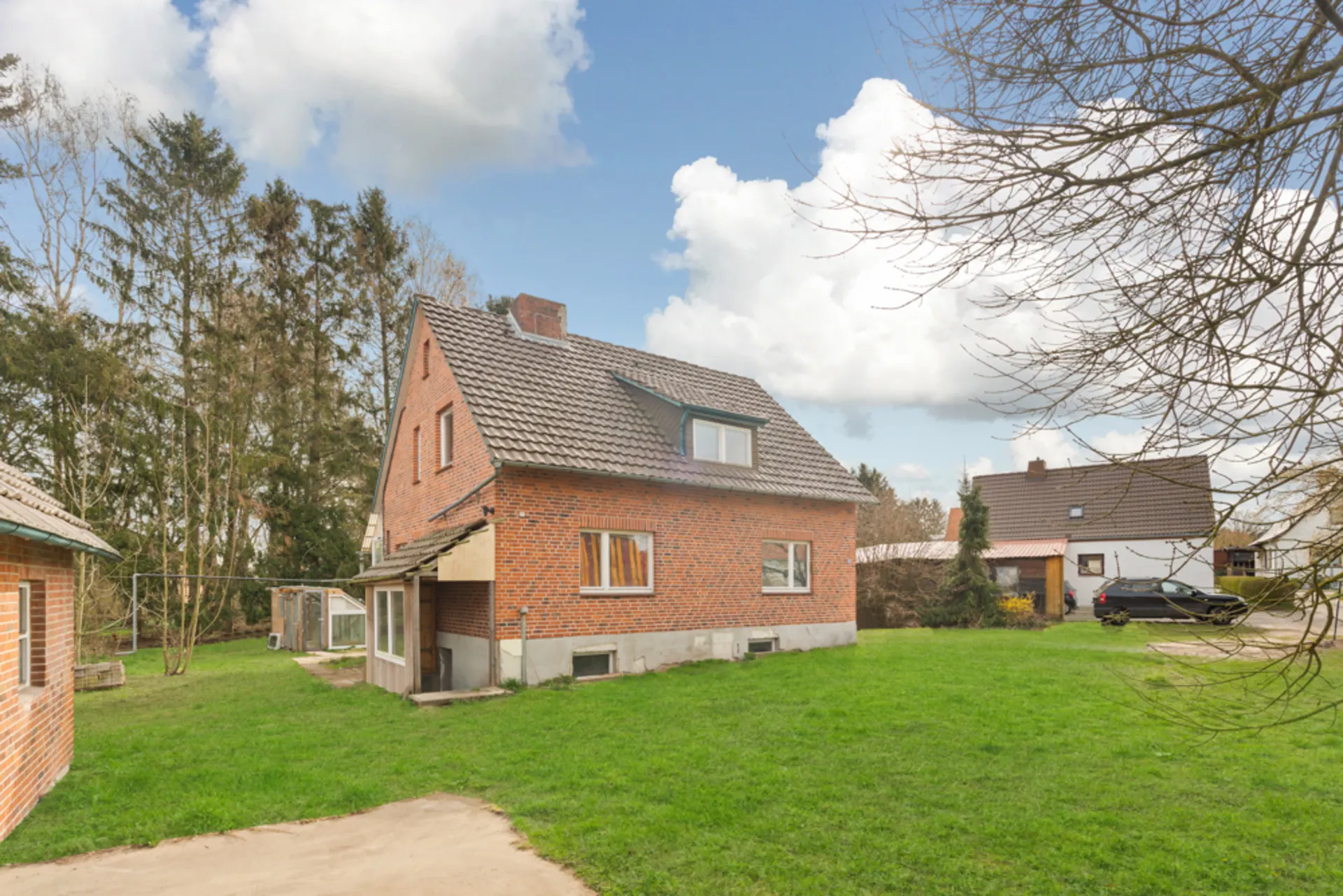 Backstein-Einfamilienhaus mit Satteldach auf grünem Grundstück, Bäume im Hintergrund.