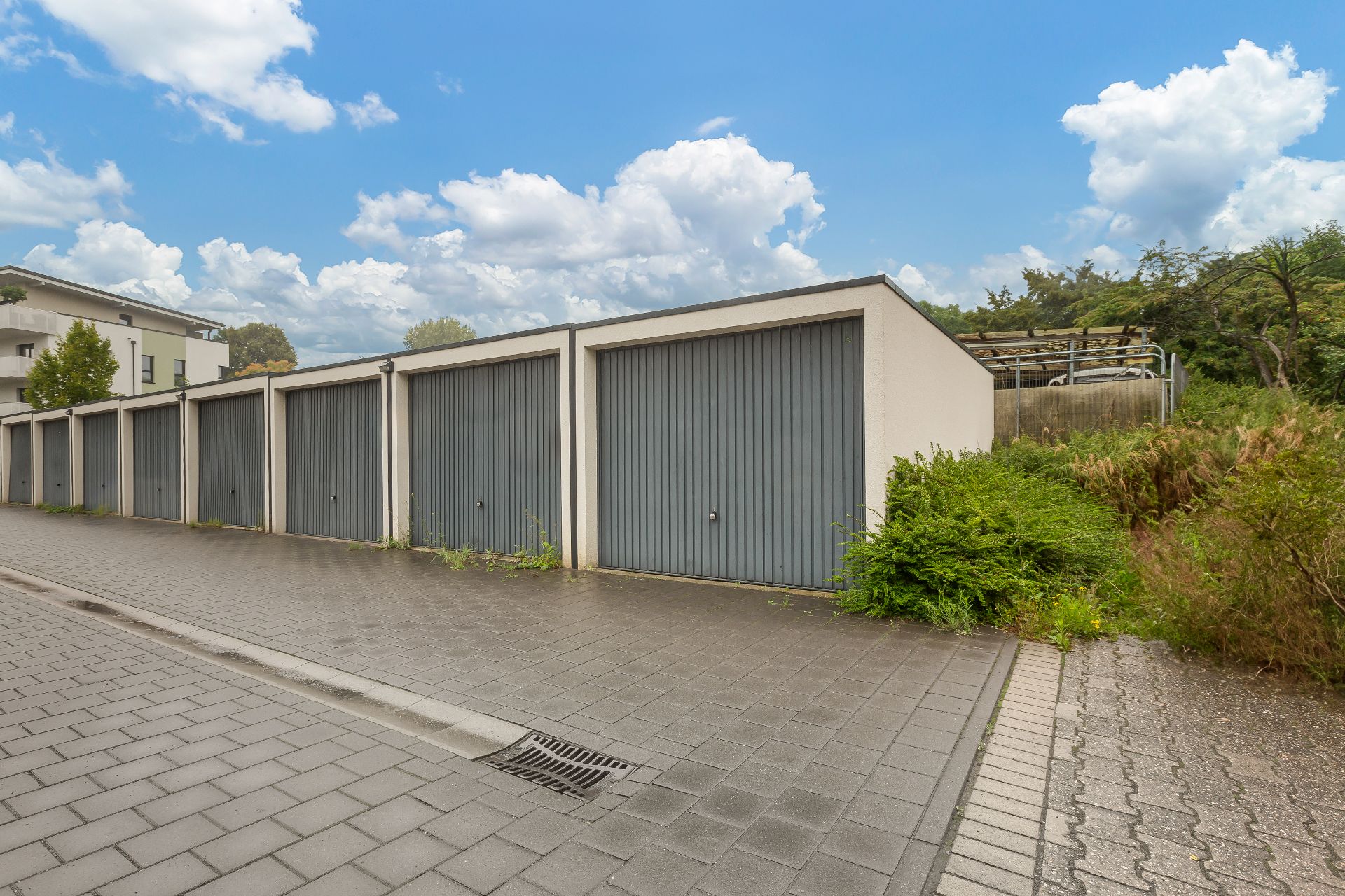 Reihe von Garagen mit grauen Toren neben einem gepflasterten Gehweg und etwas Grün.