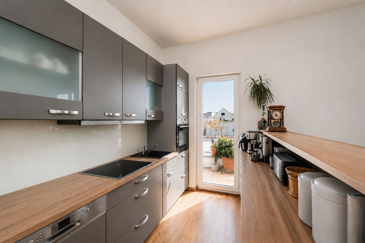 Moderne Küche mit grauen Schränken, Holzarbeitsplatten und Zugang zu einem Balkon mit Pflanzen.