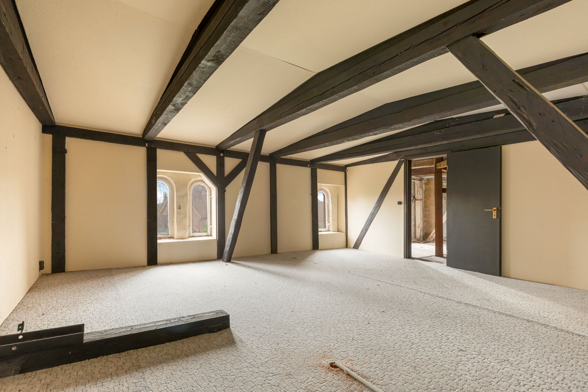 Heller Dachgeschossraum mit sichtbaren dunklen Holzbalken und Teppichboden.