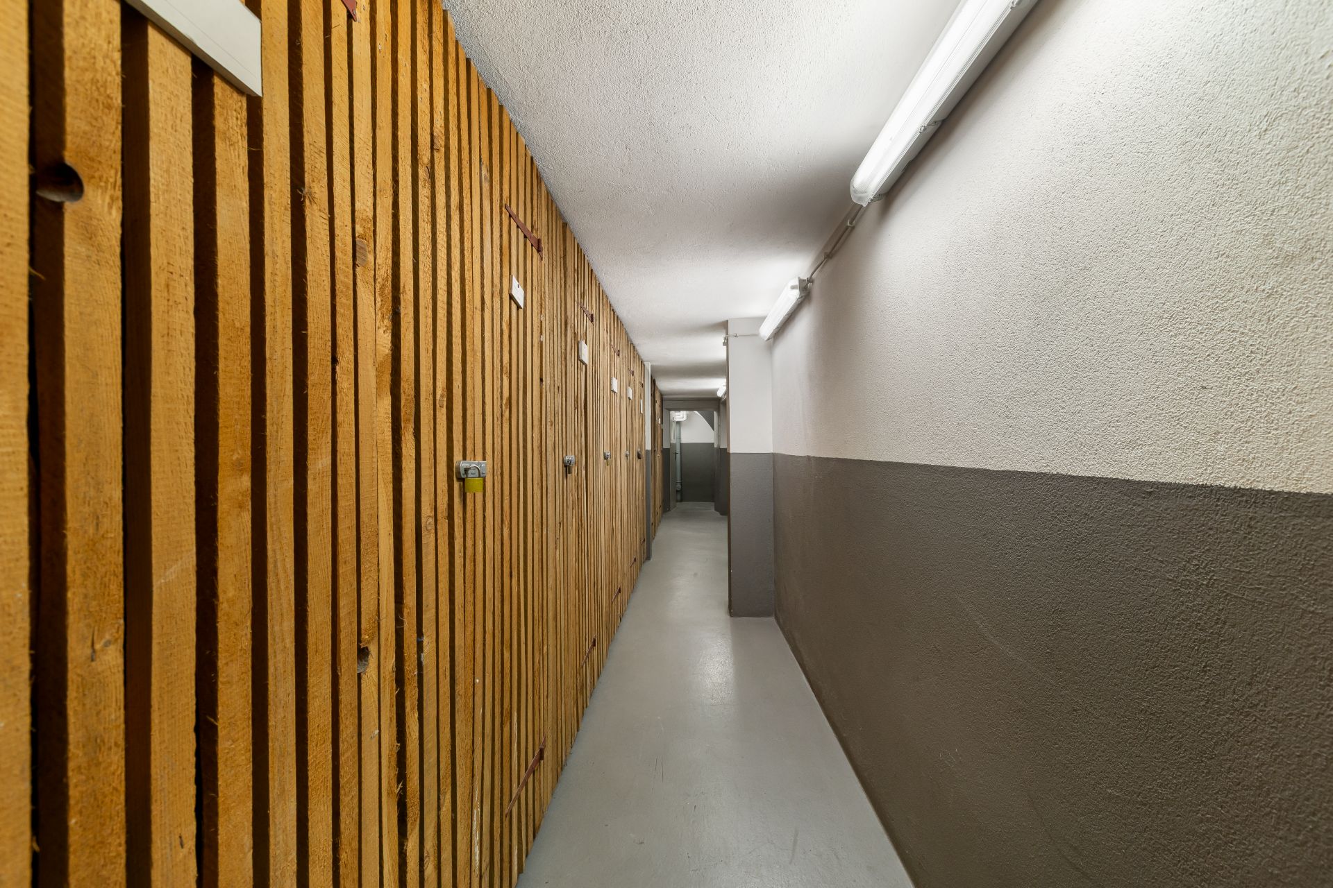 Langer, schmaler Flur mit Holzgittertüren und Beleuchtung an der Decke.
