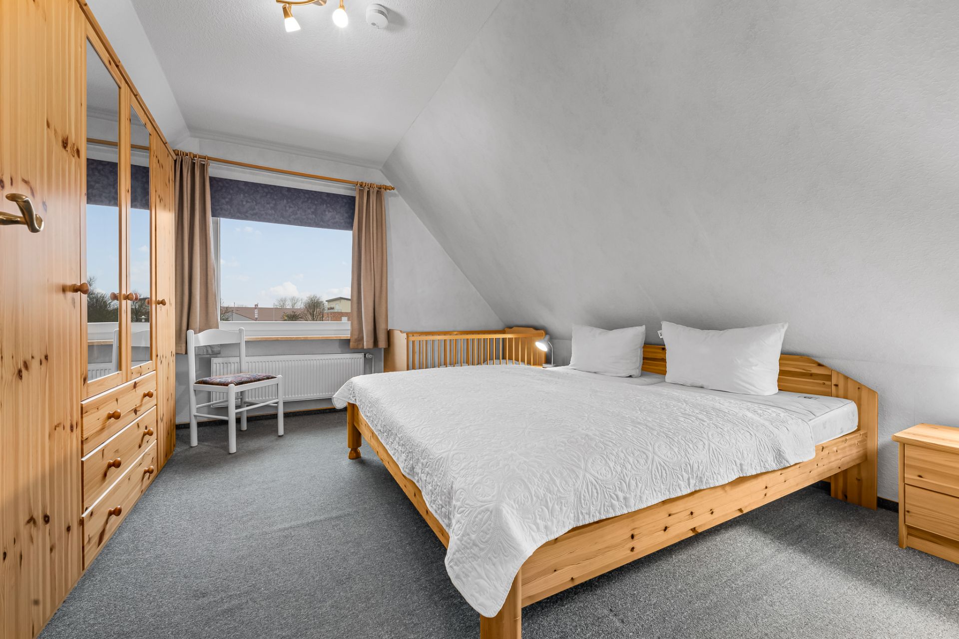 Helles Schlafzimmer mit Doppelbett, Kleiderschrank, Fenster und Holzmöbeln.