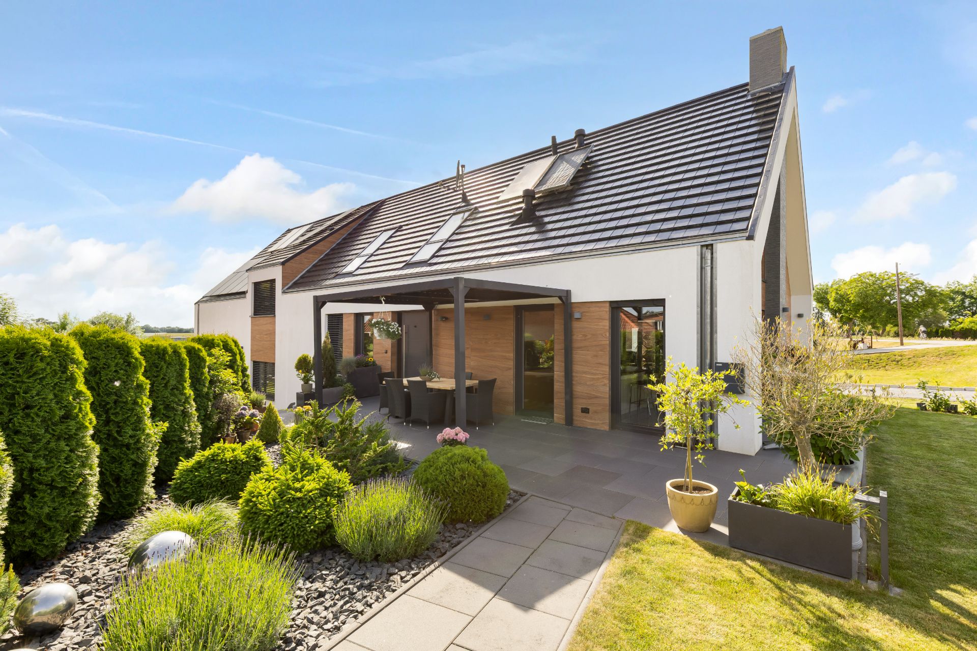 Modernes Einfamilienhaus mit Terrasse, Garten und großen Fenstern bei sonnigem Wetter.