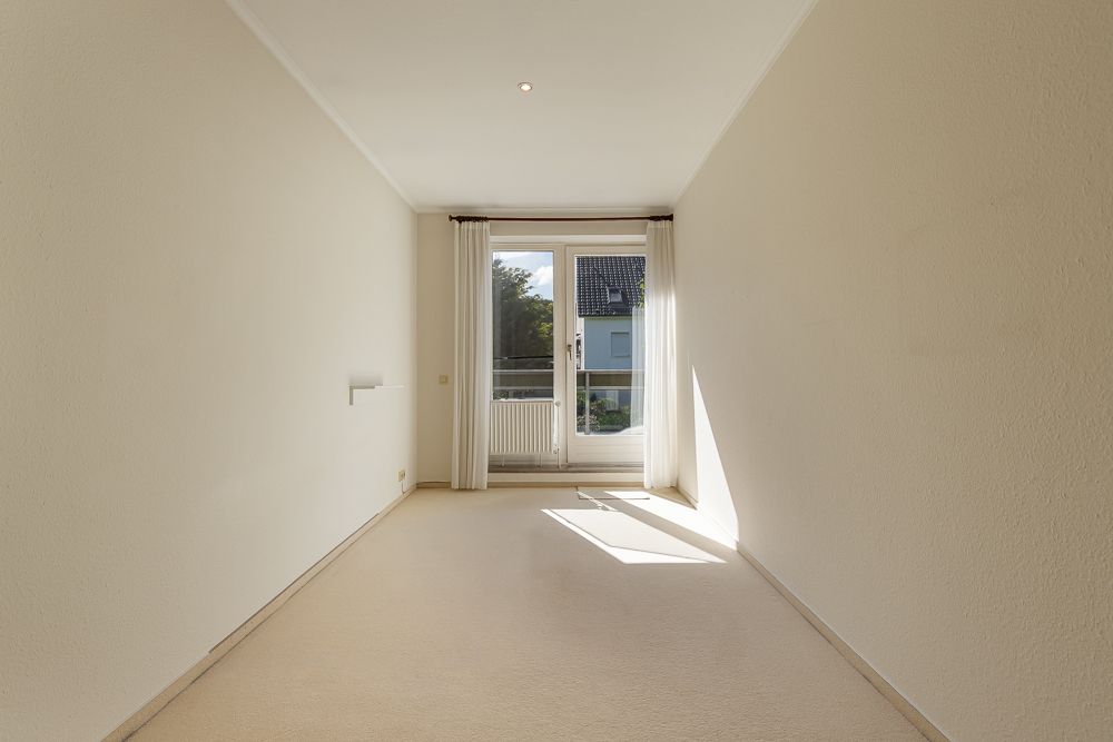 Heller, leerer Raum mit Teppichboden und großem Fenster mit Tür zum Balkon.