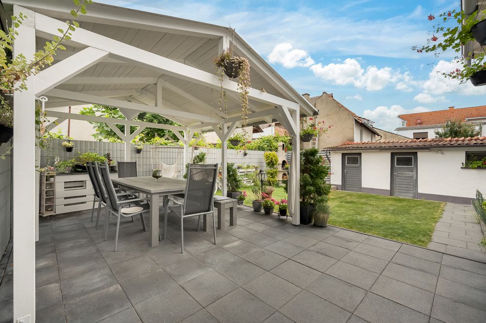 Überdachte Terrasse mit Esstisch und Stühlen, daneben ein gepflegter Garten mit Rasen.