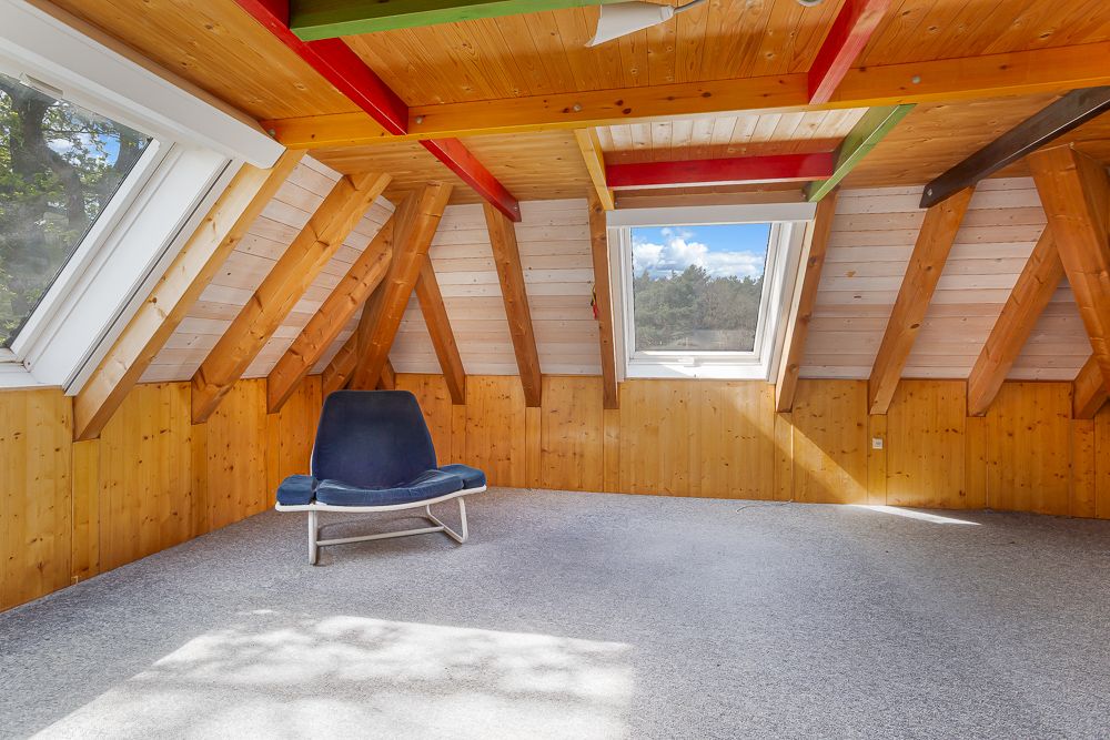 Heller Dachbodenraum mit Holzverkleidung, großen Fenstern und einem blauen Sessel.