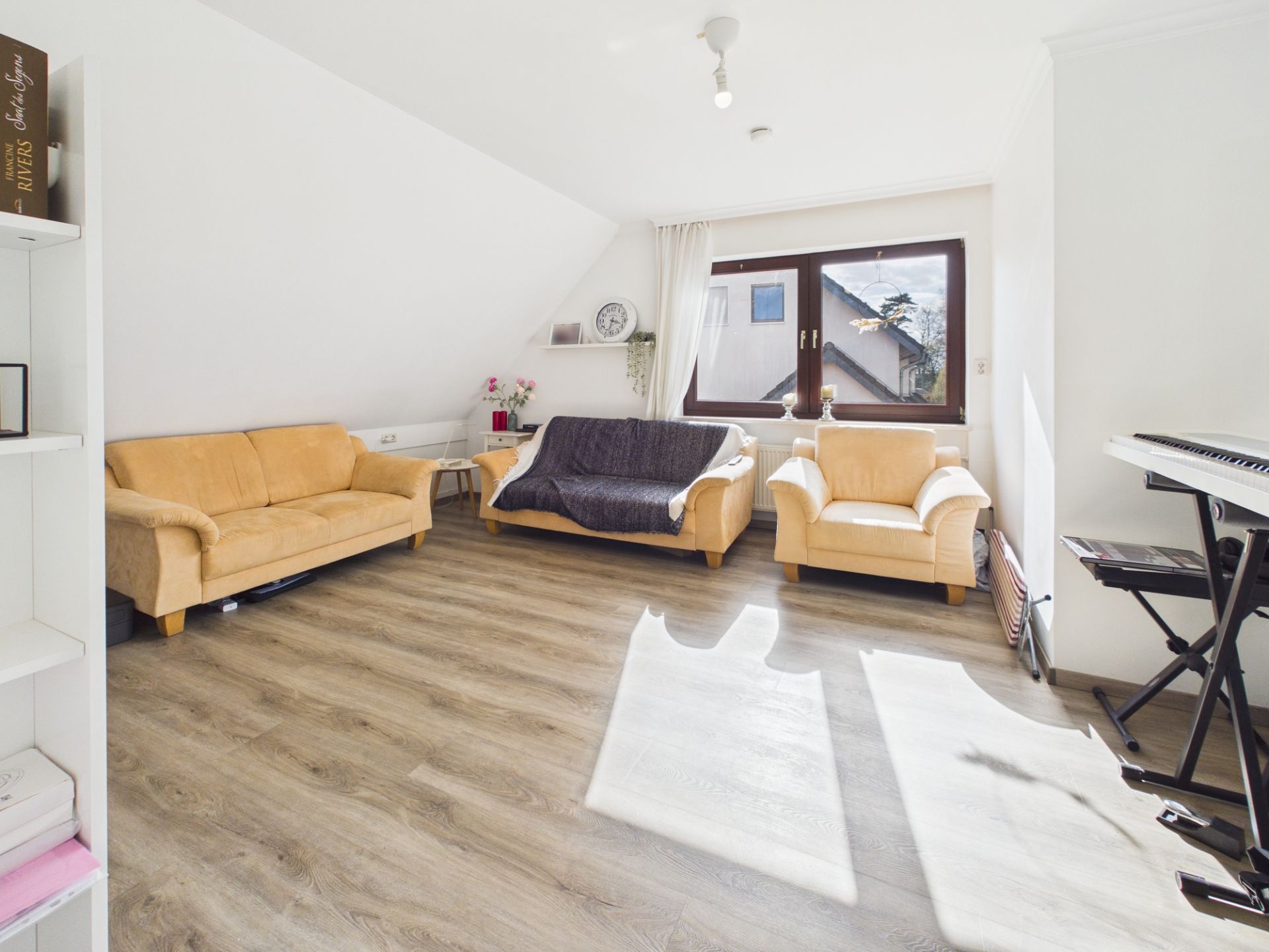 Helles Wohnzimmer mit drei Sofas, einem Fenster und einem Keyboard am Rand.