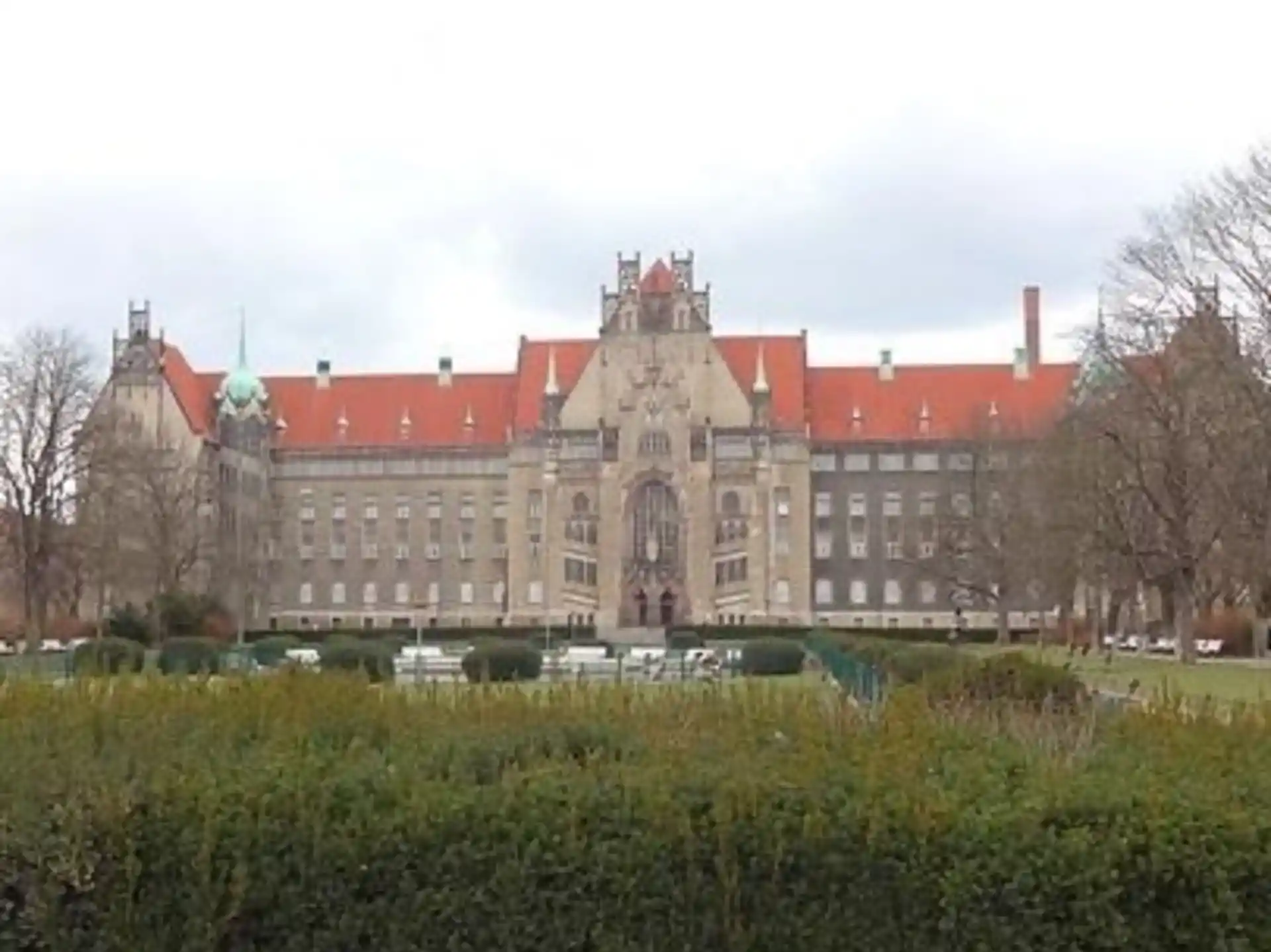 Großes historisches Gebäude mit rotem Dach und dekorativer Fassade, davor eine Gartenanlage.