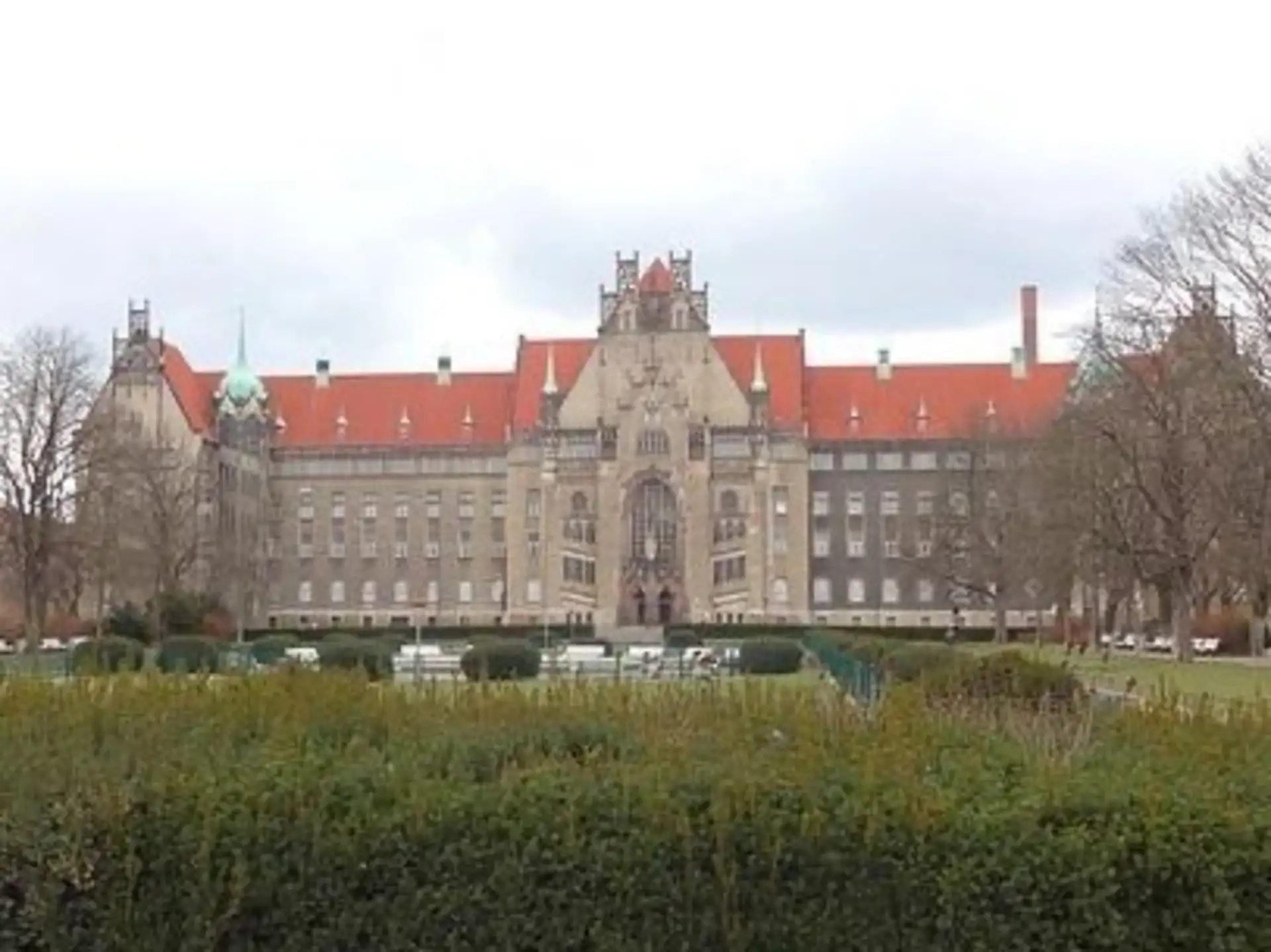 Großes historisches Gebäude mit rotem Dach und dekorativer Fassade, davor eine Gartenanlage.