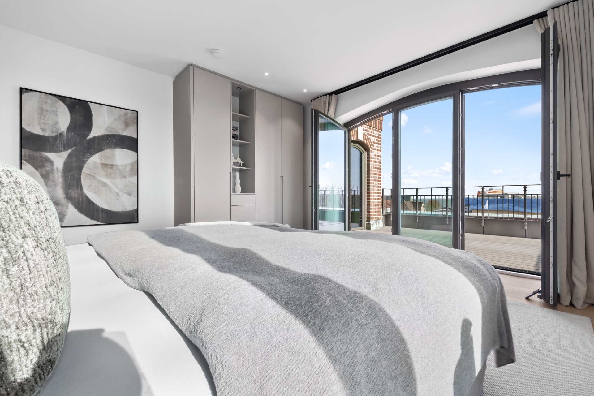 Helles Schlafzimmer mit großem Bett, Einbauschrank und Zugang zu einem Balkon mit Glasfenstern.