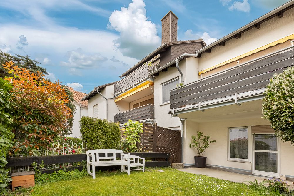 Garten mit weißer Bank, Sträuchern und Blick auf einen Balkon und Hausfassade.