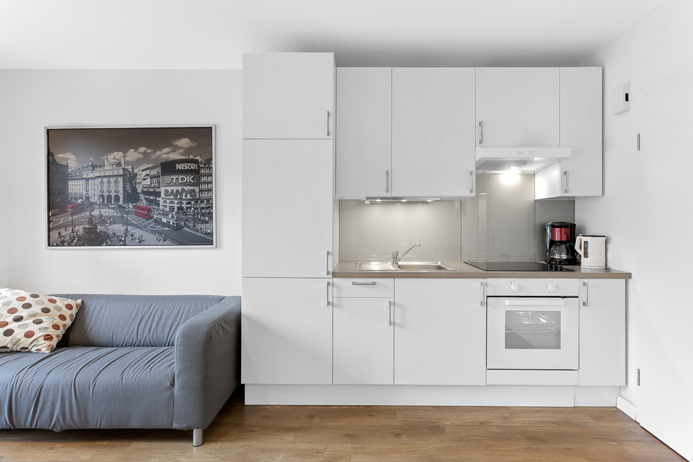 Moderne Einbauküche mit weißen Schränken, Sofa links und Wandbild im Hintergrund.
