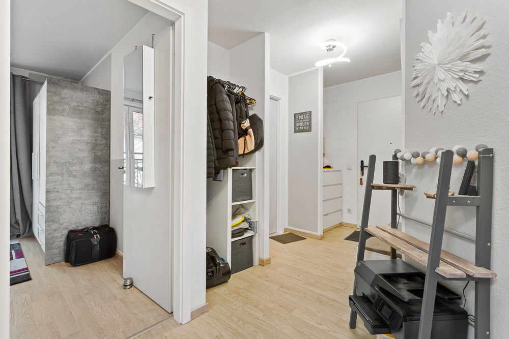 Heller Flur mit Garderobe, Regal, Wanddeko und Holzfußboden in einer Wohnung.