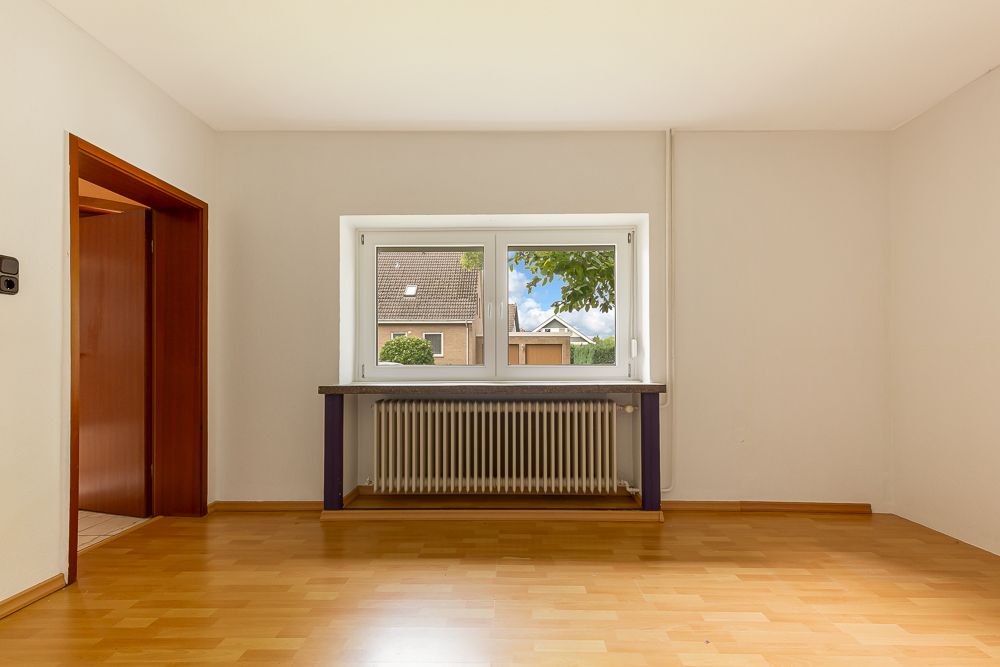 Helles leeres Zimmer mit Holzfußboden, Fenster und Heizkörper unter dem Fenster.
