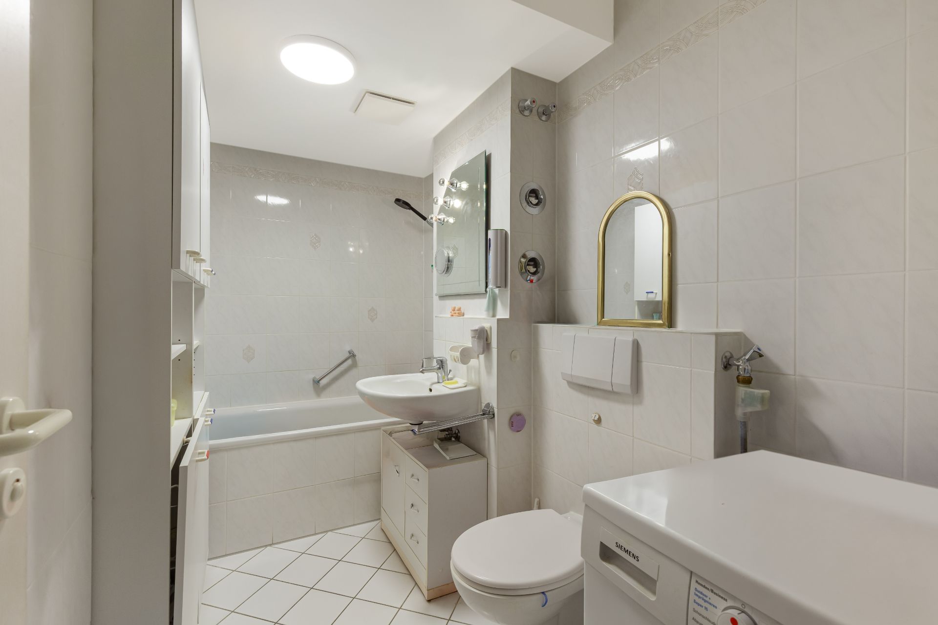 Helles Badezimmer mit Badewanne, Waschbecken, Toilette, Spiegel und Waschmaschine.