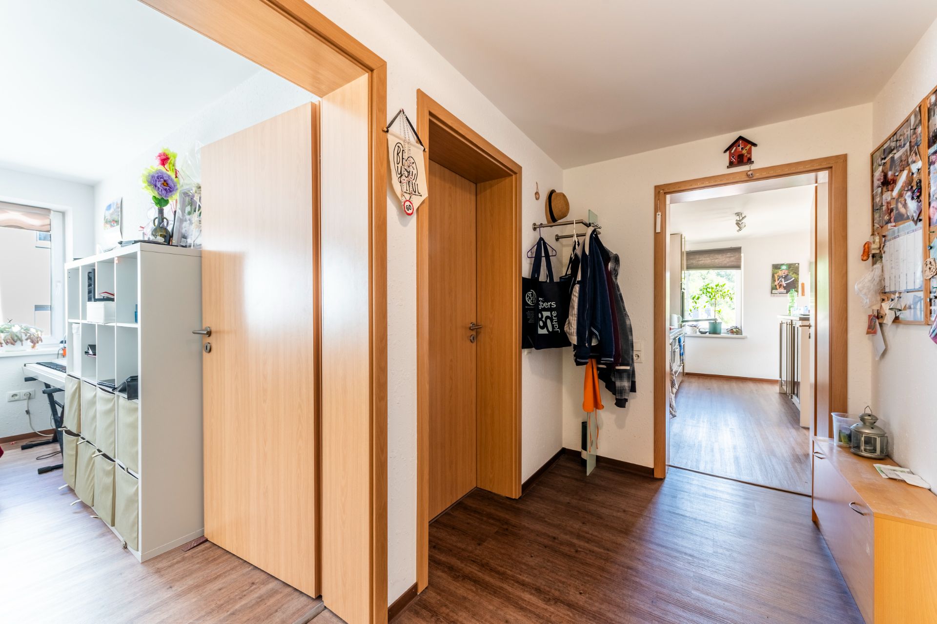 Heller Flur einer Wohnung mit Holzboden, offenen Türen und Wandgarderobe.