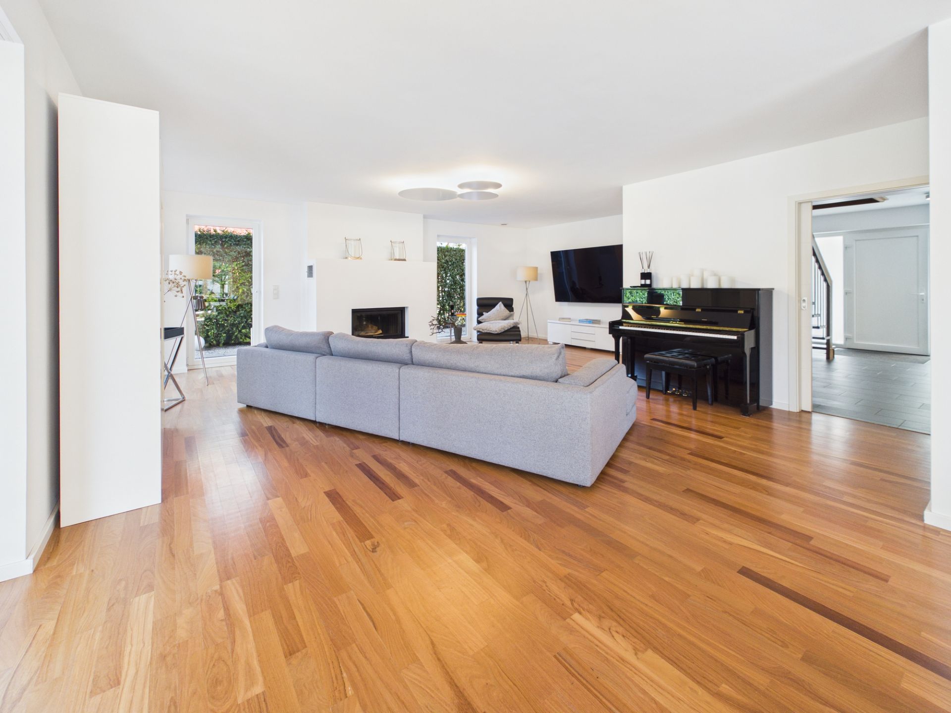 Helles Wohnzimmer mit Holzfußboden, grauem Sofa, Fernseher und Klavier.