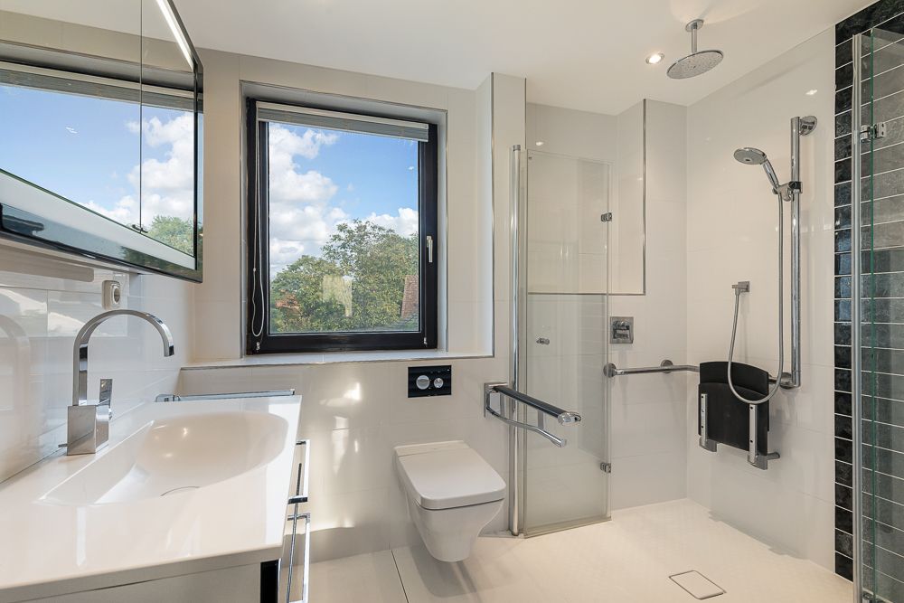 Modernes barrierefreies Badezimmer mit Dusche, WC, Waschbecken und großem Fenster.
