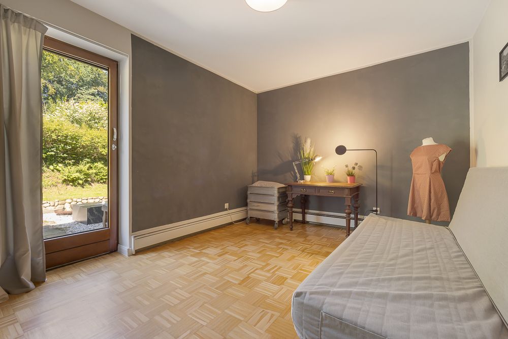 Heller Raum mit grauer Wand, Sofa, Schreibtisch, Pflanzen und Tür zum Garten.