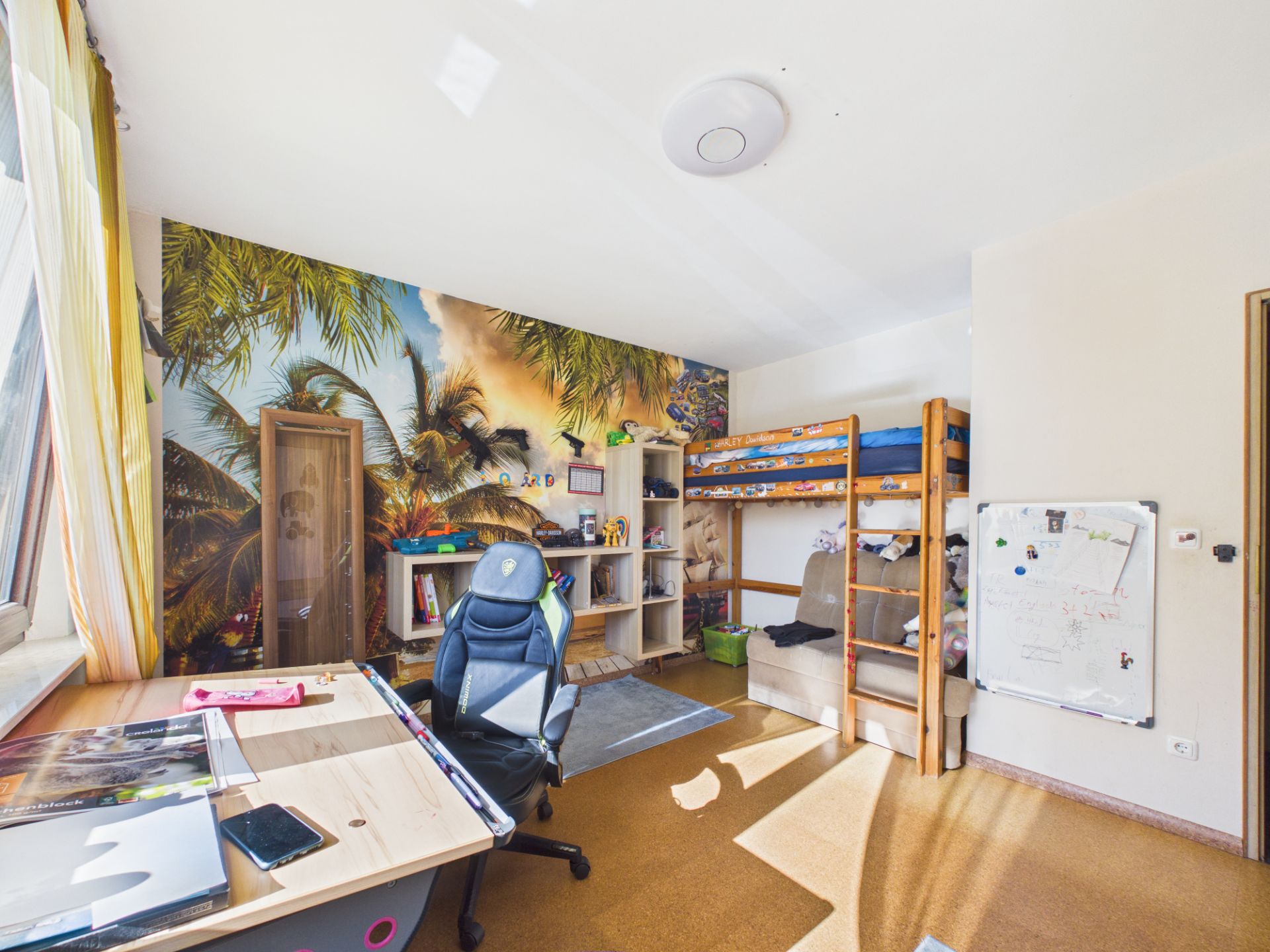 Helles Kinderzimmer mit Hochbett, Schreibtisch und bunter Palmentapete.