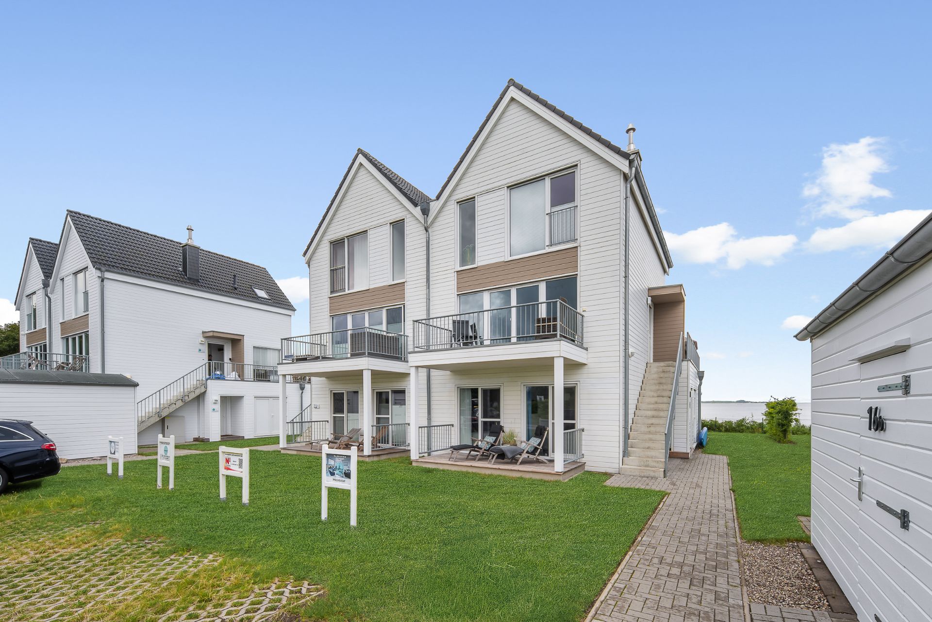 Zwei moderne Doppelhaushälften mit Balkonen, Terrasse und Grünfläche davor.