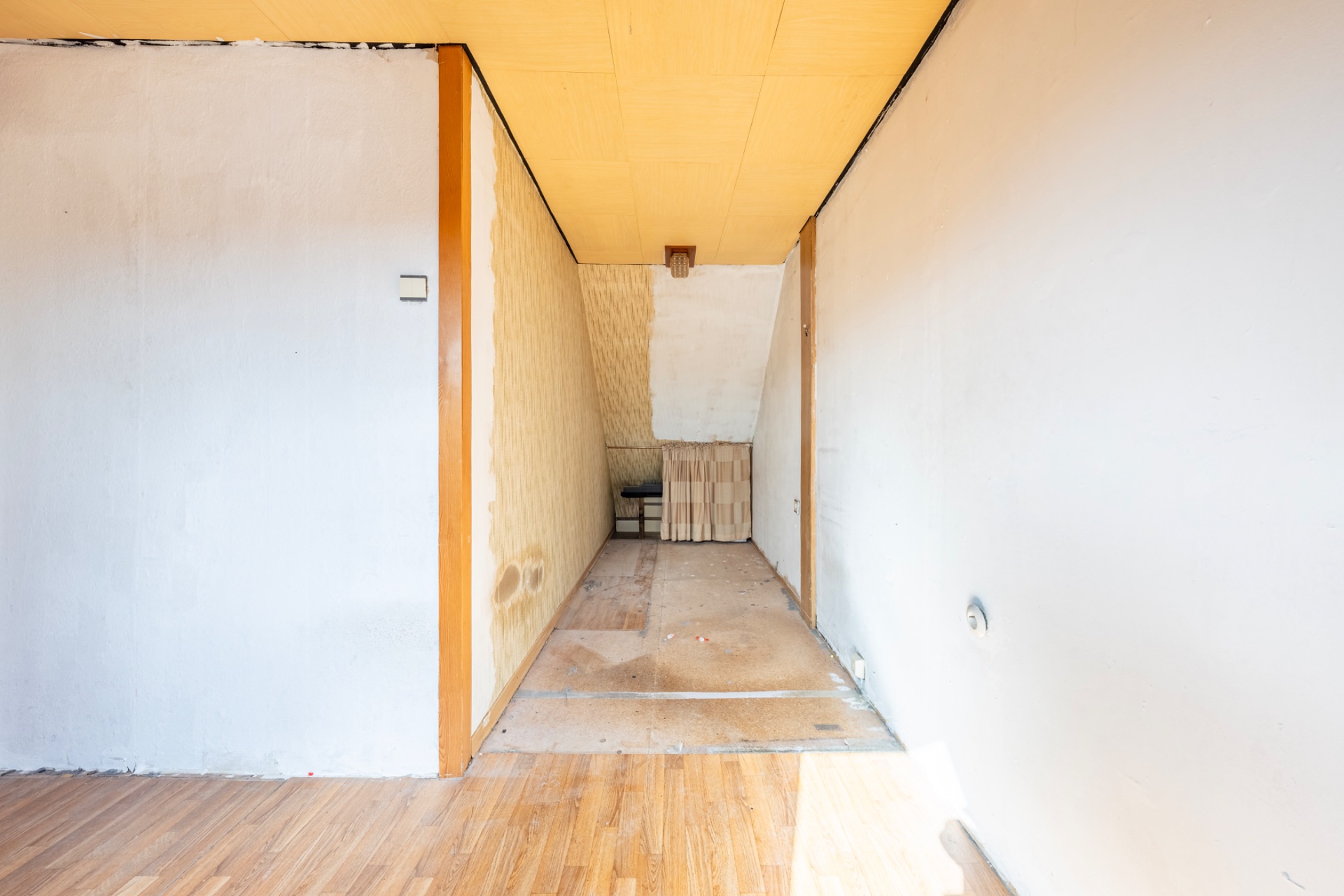 Schmaler, leerer Flur mit Holzdecke und sichtbaren Gebrauchsspuren an Wänden und Boden.