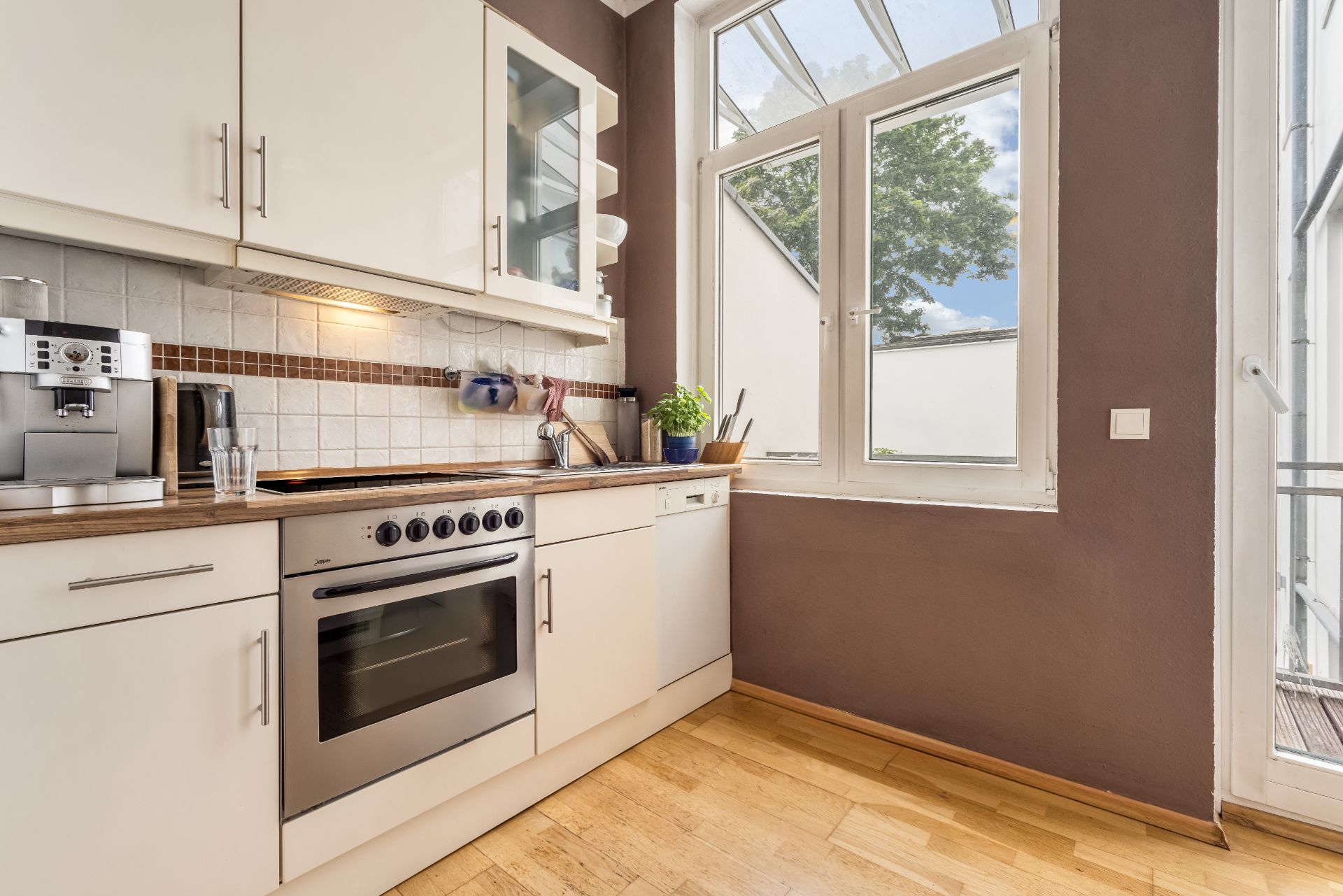 Moderne Küche mit weißen Schränken, Herd, Spülmaschine und großem Fenster.