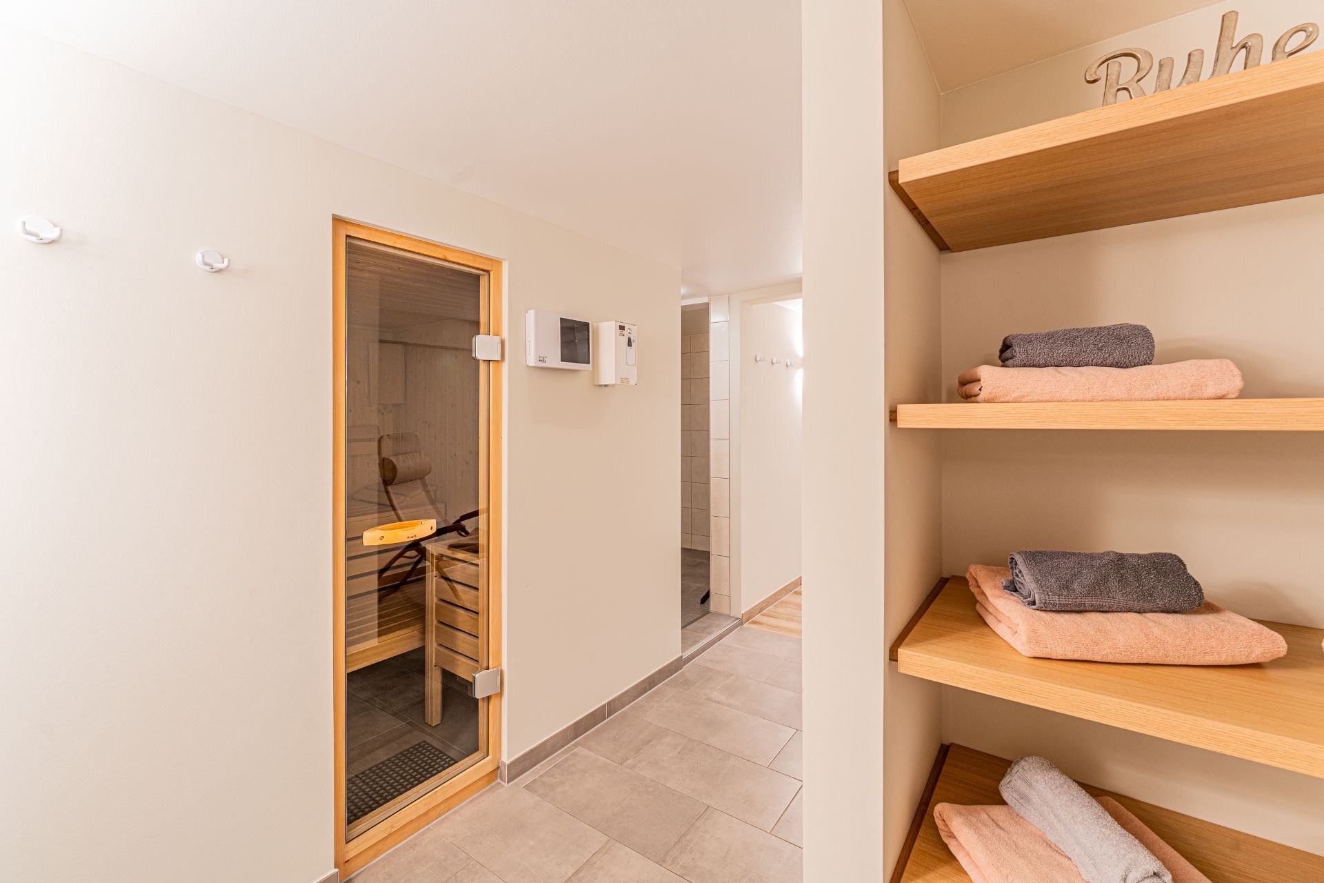 Saunaraum mit Glastür und Regal mit gefalteten Handtüchern an der Wand.
