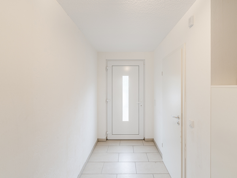 Heller Flur mit weißer Haustür, einer Seitentür und Fliesenboden.