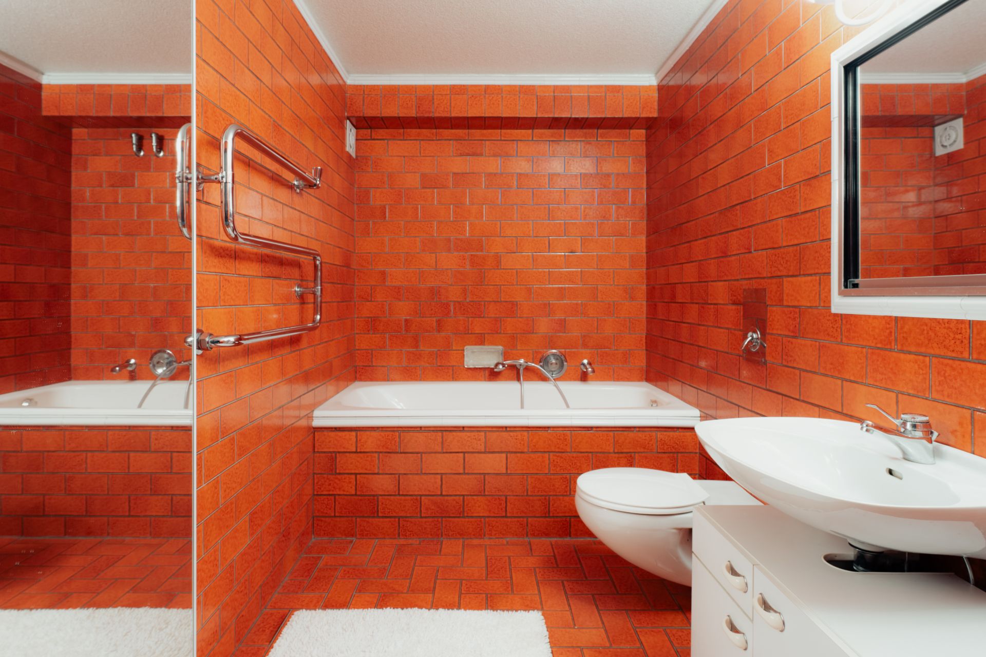 Badezimmer mit orangefarbenen Fliesen, Badewanne, Waschbecken, Spiegel und WC.