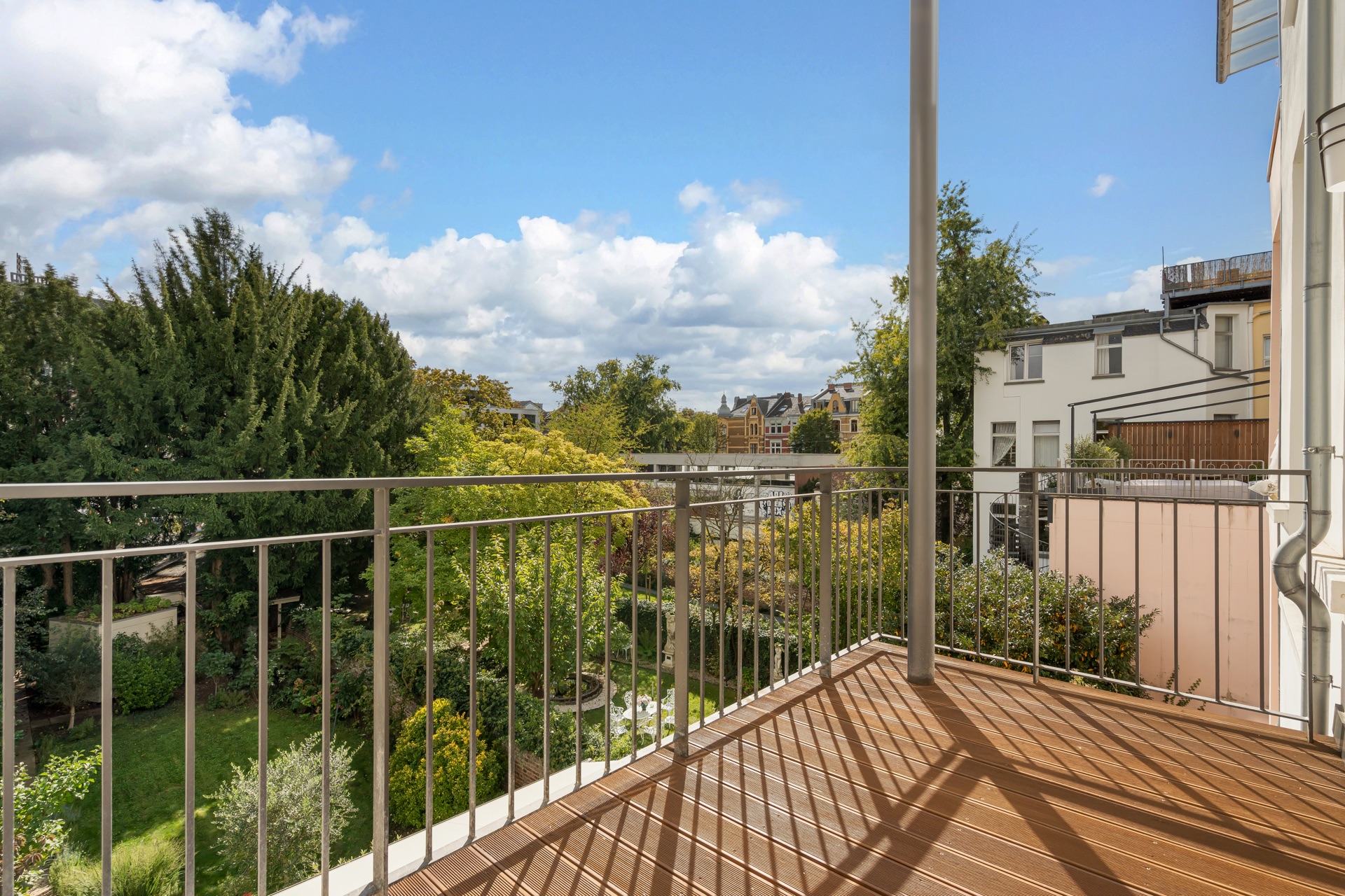 Balkon mit Metallgeländer und Blick auf einen grünen Garten und benachbarte Häuser.