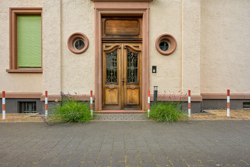 Holztür mit Verzierungen, zwei runden Fenstern und grünem Fensterladen an einem Wohnhaus.