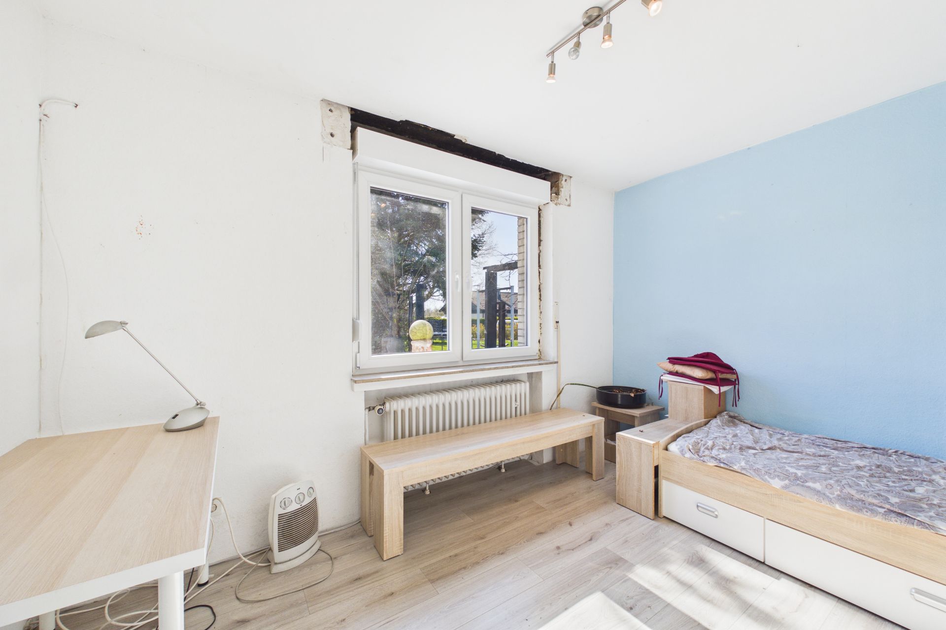 Helles Schlafzimmer mit Schreibtisch, Einzelbett und großem Fenster.