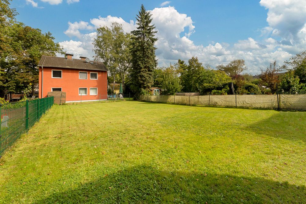 Großer grüner Garten mit Rasen, Zaun und einem roten Wohnhaus im Hintergrund.