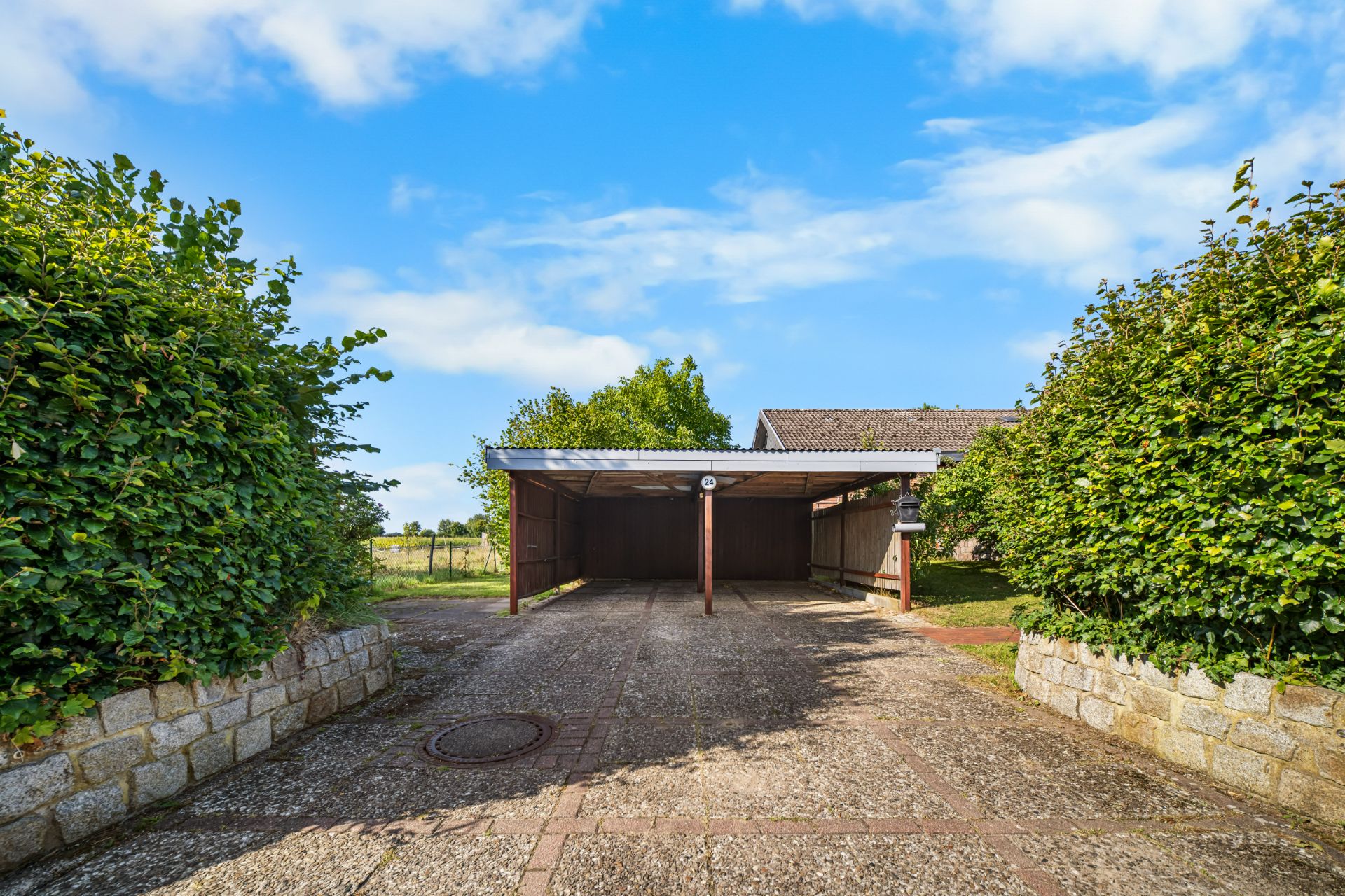 Überdachter Carport mit zwei Parkplätzen, umgeben von Hecken und Steinmauern.