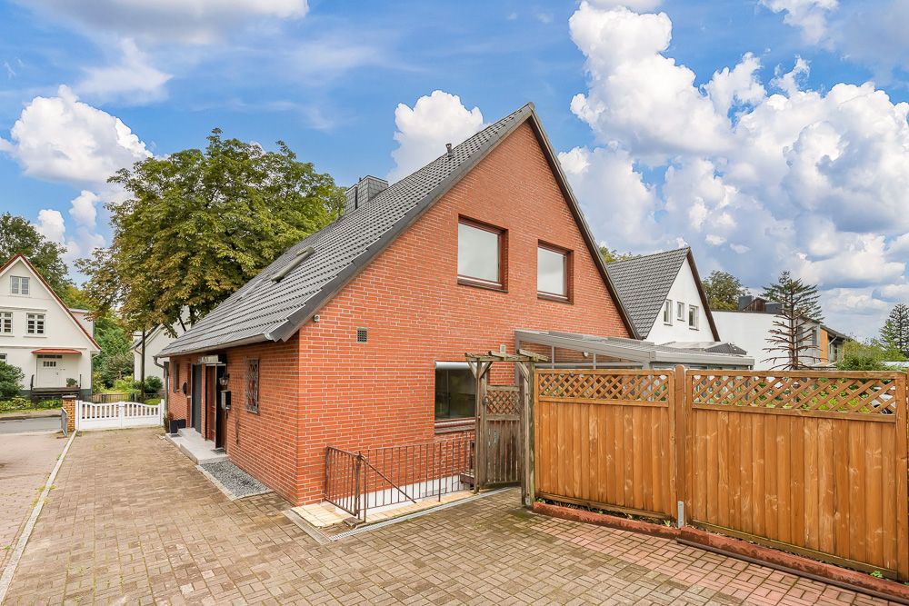 Backstein-Einfamilienhaus mit Satteldach, Auffahrt und Holzzaun im Vordergrund.