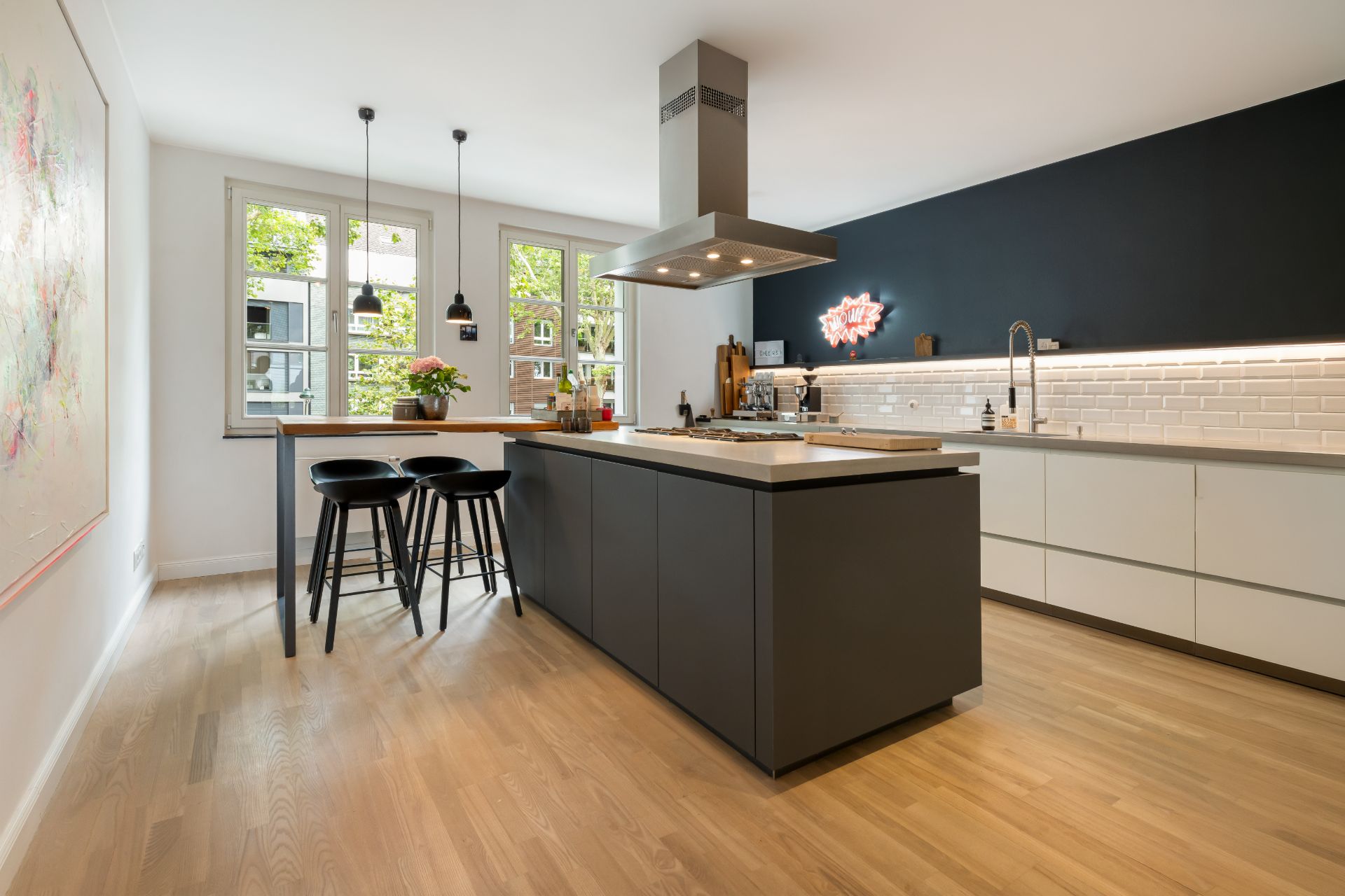 Moderne Küche mit Kücheninsel, Barhockern, Holzfußboden und großen Fenstern.