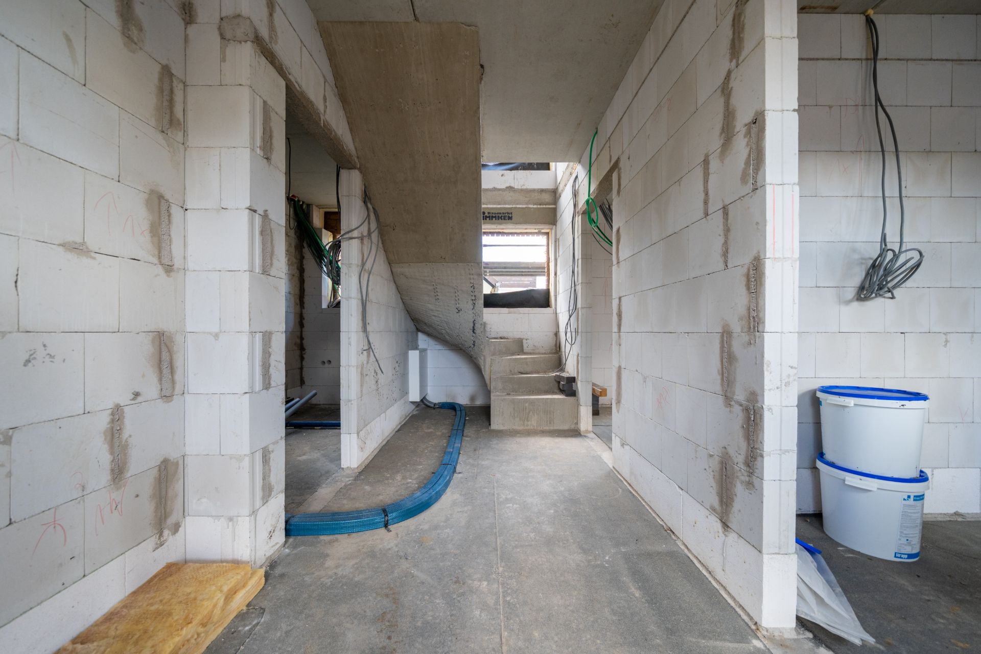 Rohbau eines Wohnhauses mit Treppe, Kabeln und Farbeimern.