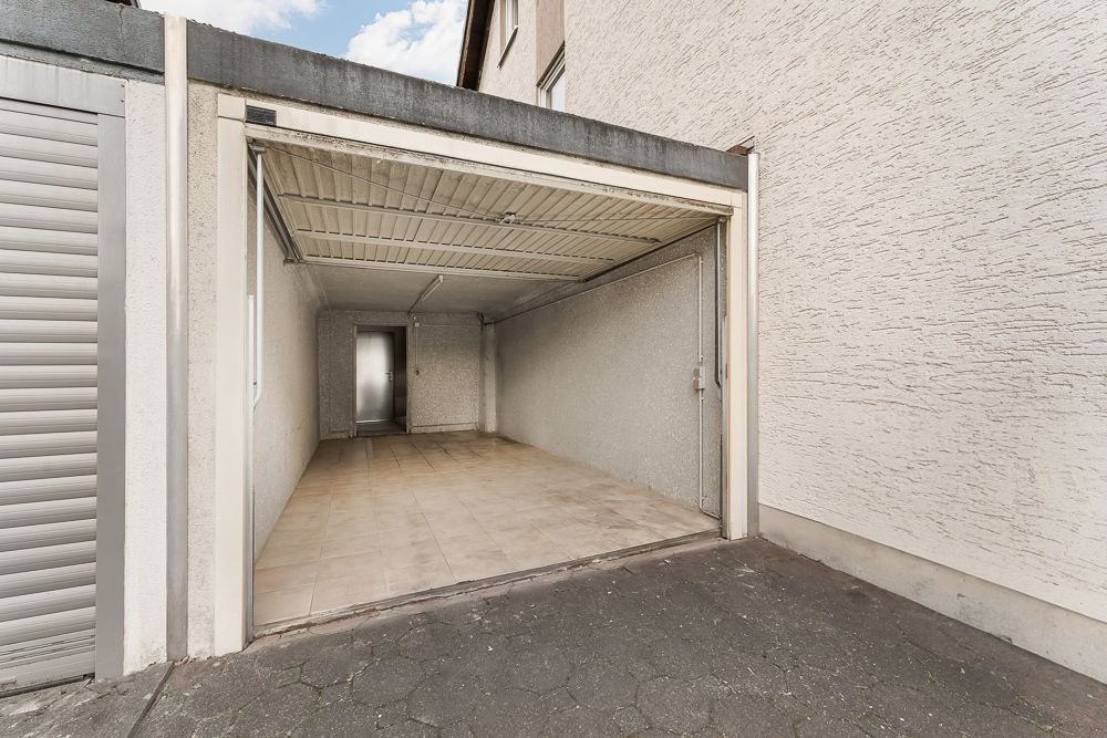 Leere Garage mit offenem Tor, gefliestem Boden und einer Tür am hinteren Ende.