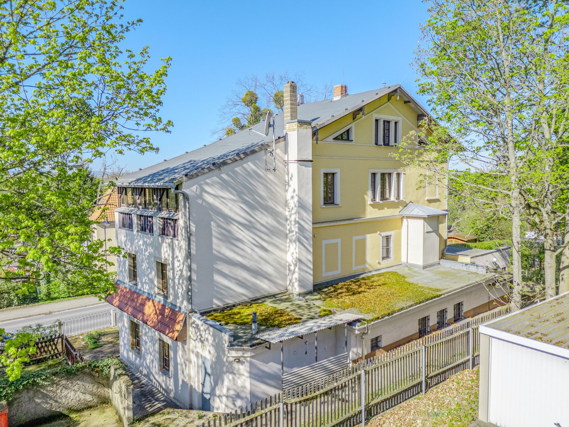 Gelbes Wohnhaus mit mehreren Stockwerken, Flachdach und Bäumen im Vorgarten.