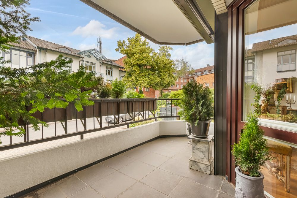 Balkon mit Fliesenboden, Pflanzen in Töpfen und Blick auf Straße und Wohngebäude.